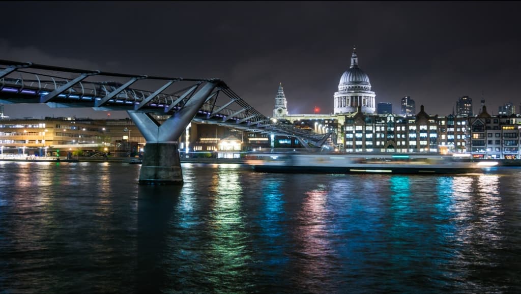 London Millennium Bridge and St Paul's Cathedral at night, with the Thames reflecting city lights